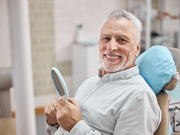 Senior man sitting in dental chair and holding mirror