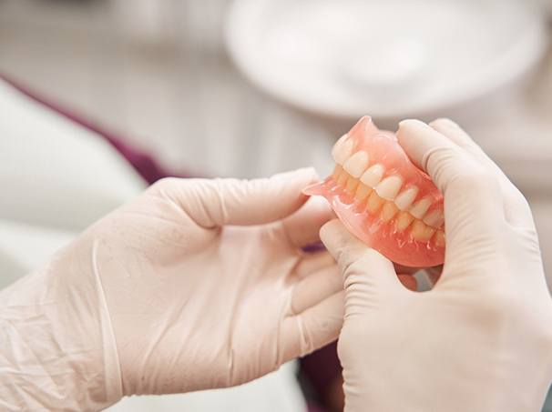 A dentist holding dentures in their gloved hands