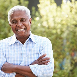 Man crossing his arms and smiling with greenery in the background