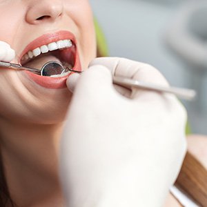 Nose-to-shoulder view of woman having mouth examined by dentist in white gloves