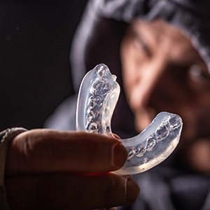 Man in hoodie holding clear mouthguard
