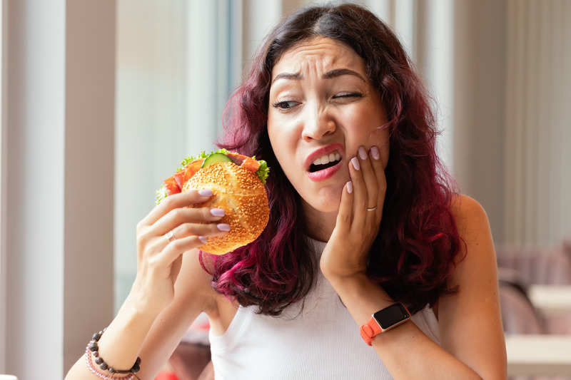 Patient eating burger and holding their cheek due to jaw pain