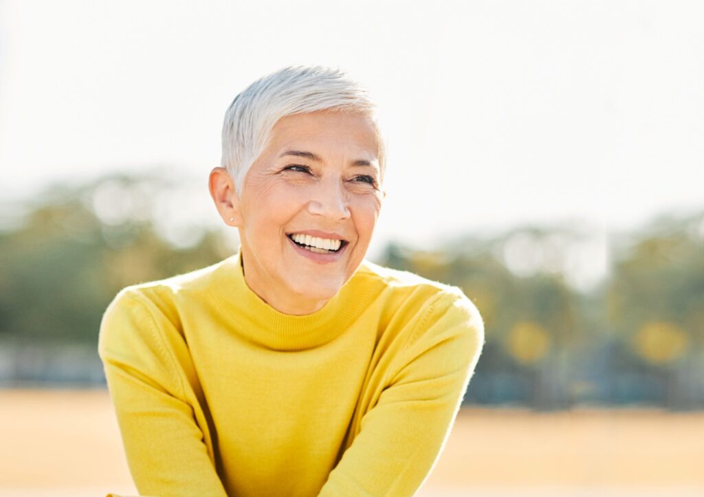 Woman with short white hair in yellow sweater outside smiling