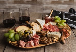 Charcuterie board with meats, grapes, crackers, and cheese next to 2 glasses of red wine